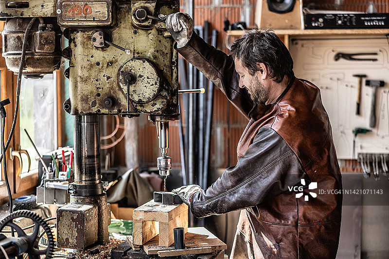 在旧车间用液压钻在金属部件上钻孔的男人图片素材