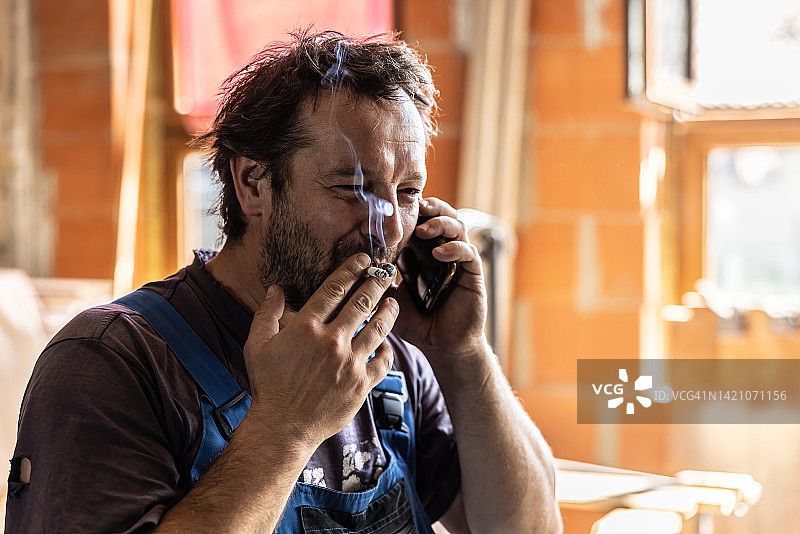 工地上，手工艺人抽着烟打电话图片素材