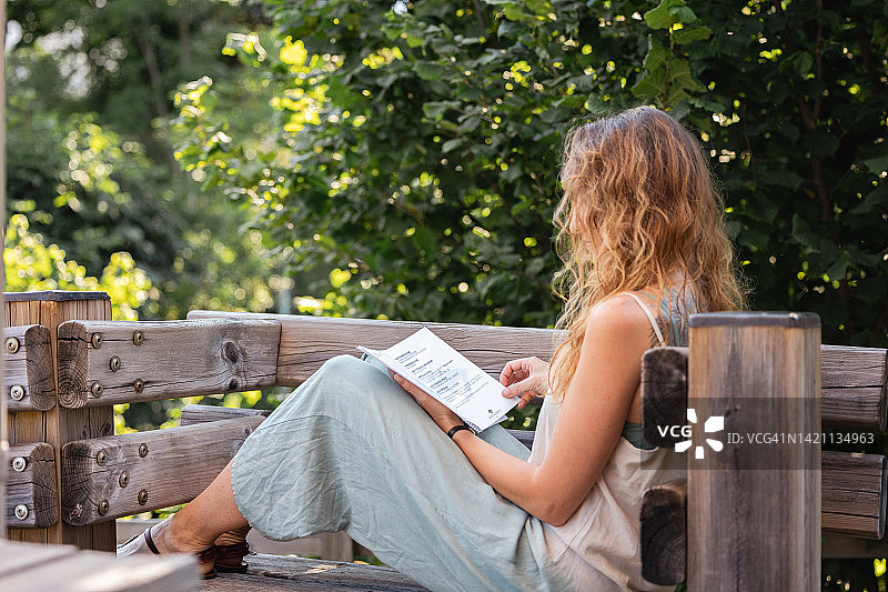 年轻女人坐在花园的木凳上看书图片素材