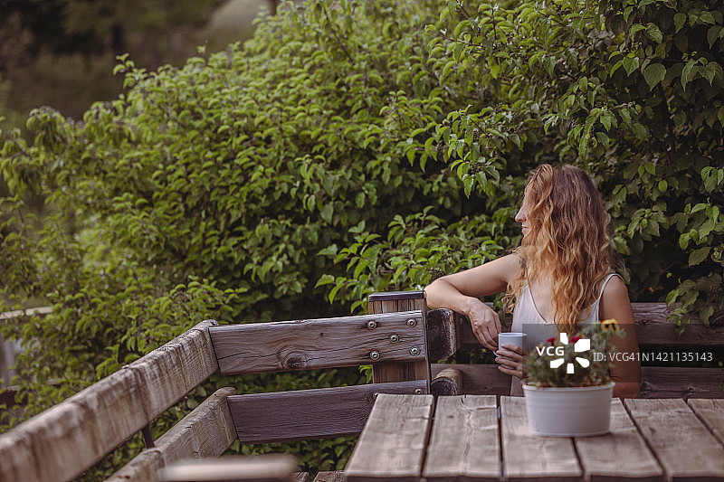 年轻女游客在度假村花园里享受夏日清晨，品茶一杯图片素材