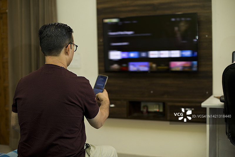 男子在家中客厅边看电视边使用手机图片素材