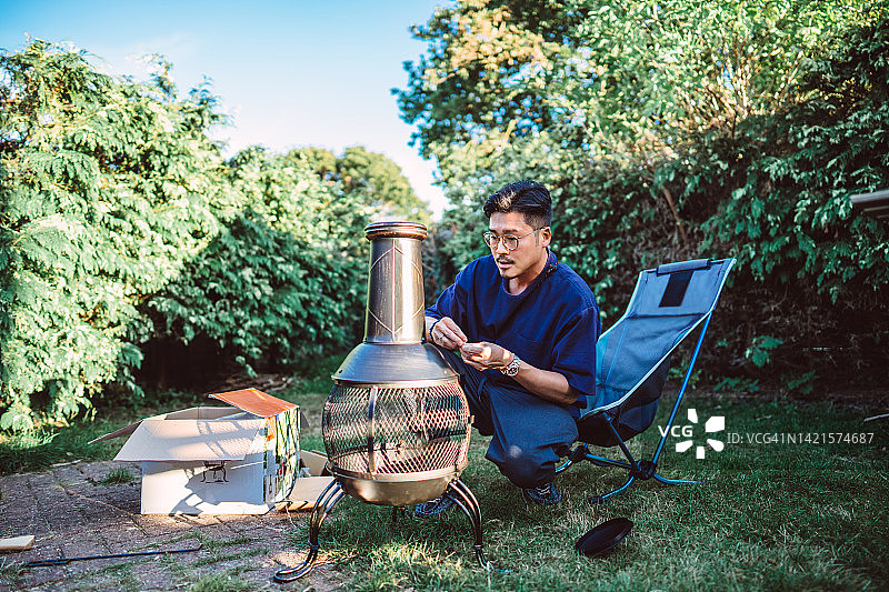 年轻帅气的男人在家中花园里拆卸并组装户外火炉图片素材