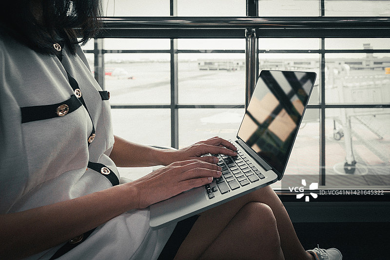 在机场使用笔记本电脑的年轻女人。在候机厅等待航班的年轻女性乘客。图片素材