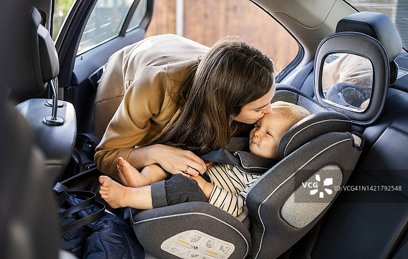 充满爱意的母亲亲吻坐在汽车安全座椅上的儿子图片素材