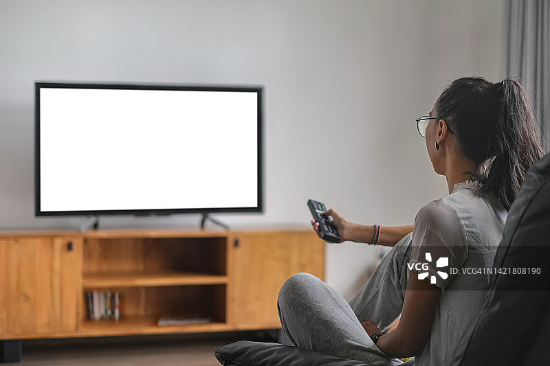 中年印度尼西亚妇女用遥控器换频道看电视图片素材