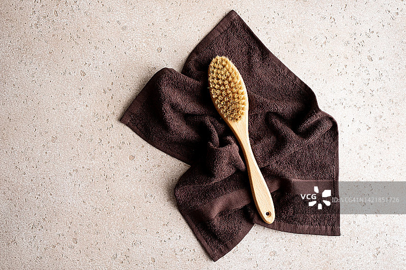 用于干刷按摩的木制身体刷和混凝土背景上的浴巾，俯视图。家庭水疗概念。零浪费。平放。复制空间。图片素材