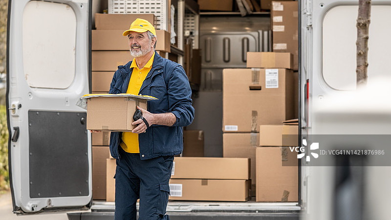 穿制服的快递员搬运纸板箱，卸载送货卡车图片素材