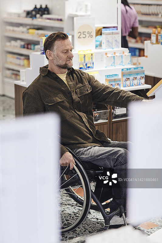 坐在轮椅上在药房使用代币机的中年男人图片素材