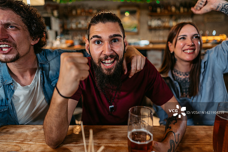 在酒吧观看体育比赛并为球队加油的年轻男人图片素材