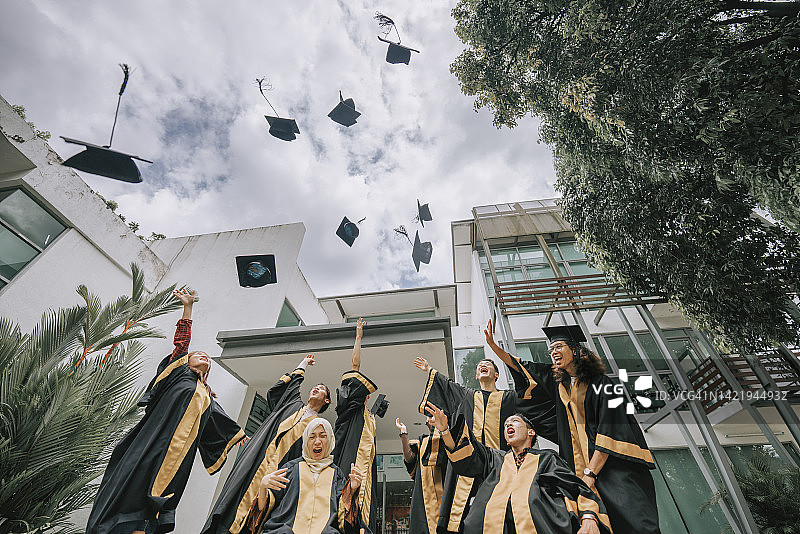 毕业日传统：兴奋的亚洲大学生低角度抛掷学士帽图片素材
