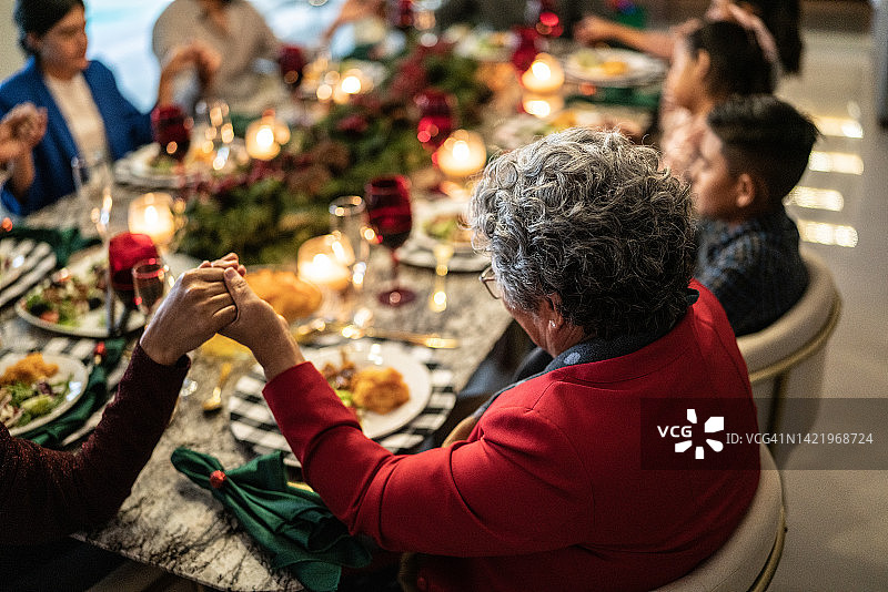 年长的女人和家人在圣诞节在家里的餐桌上祈祷图片素材
