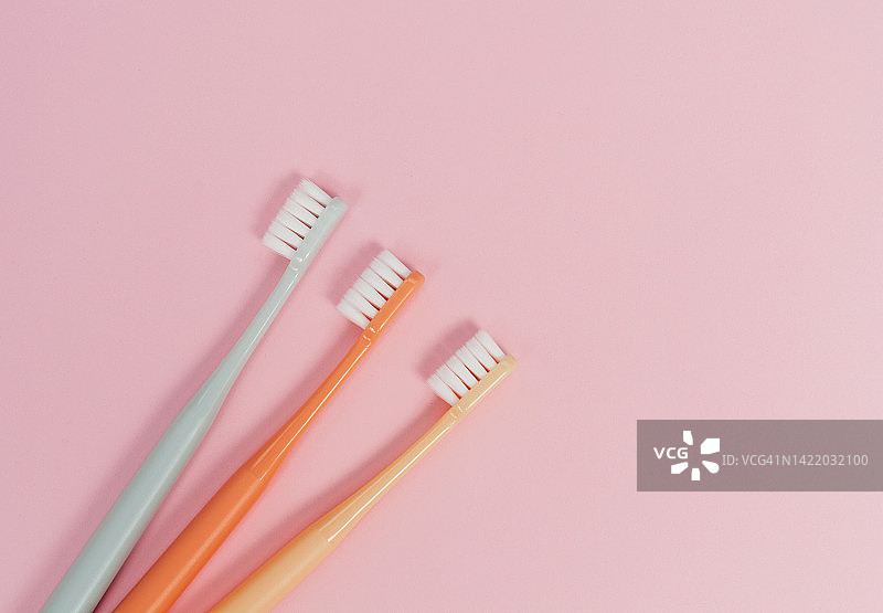 粉色背景上的三个彩色软毛牙刷图片素材