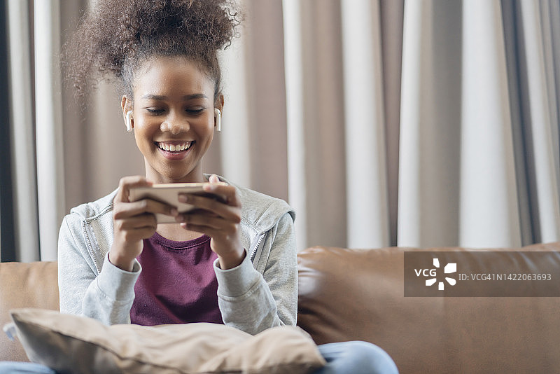 玩在线游戏的非裔美国人，在客厅里用智能手机玩在线游戏图片素材