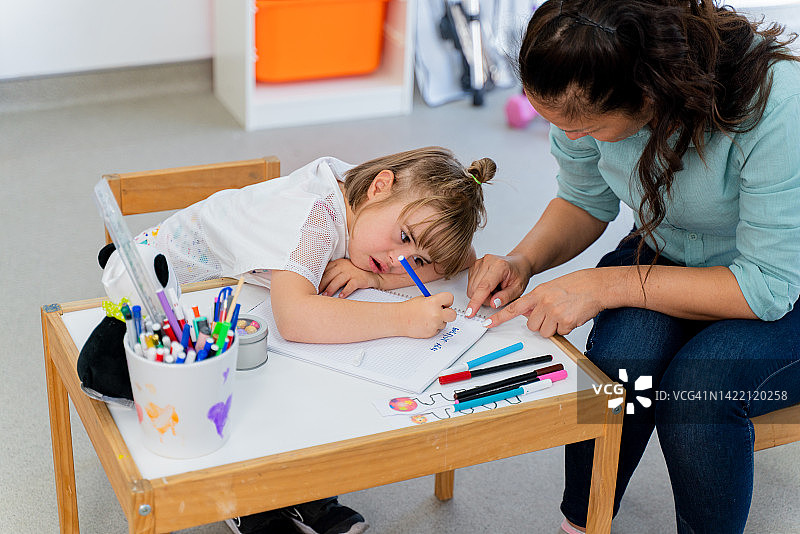 年轻女教师与坐在课桌前的唐氏综合征女学生一起工作图片素材