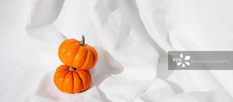 时尚简约的构图，白色织物上放着小南瓜。秋季氛围。感恩节。你好，秋天。万圣节。节日背景。生态。环保。图片素材