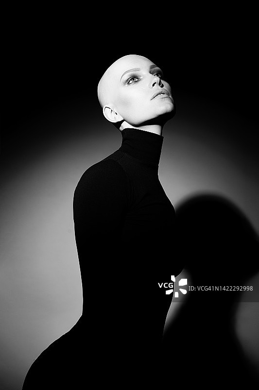 患有脱发的年轻女子，在黑色背景的聚光灯下。没有头发、睫毛和眉毛的美丽女士的黑白肖像图片素材