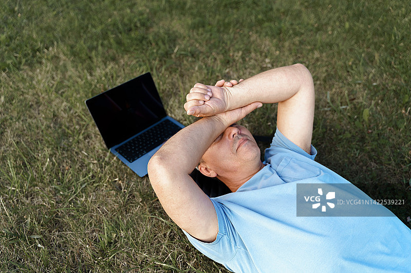 在户外绿地上放松、使用笔记本电脑的中年男人图片素材