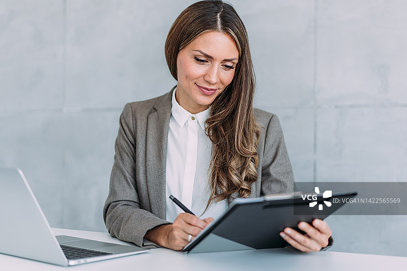 自信的女商人使用笔记本电脑并做笔记图片素材
