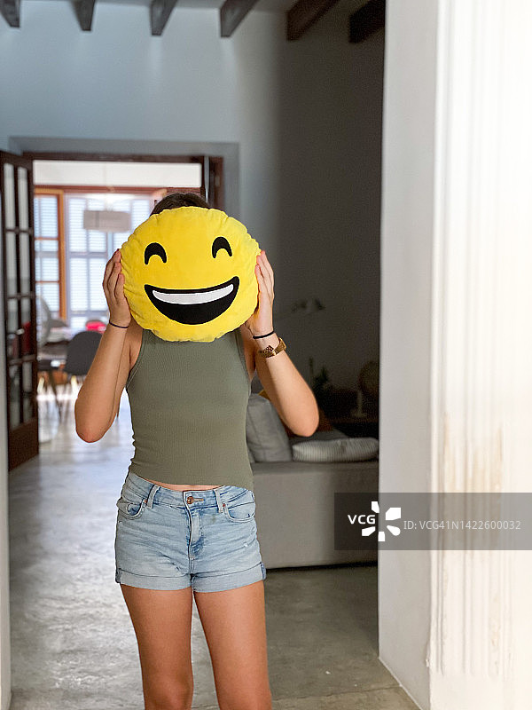 世界微笑日：手持微笑表情靠垫的年轻女孩图片素材