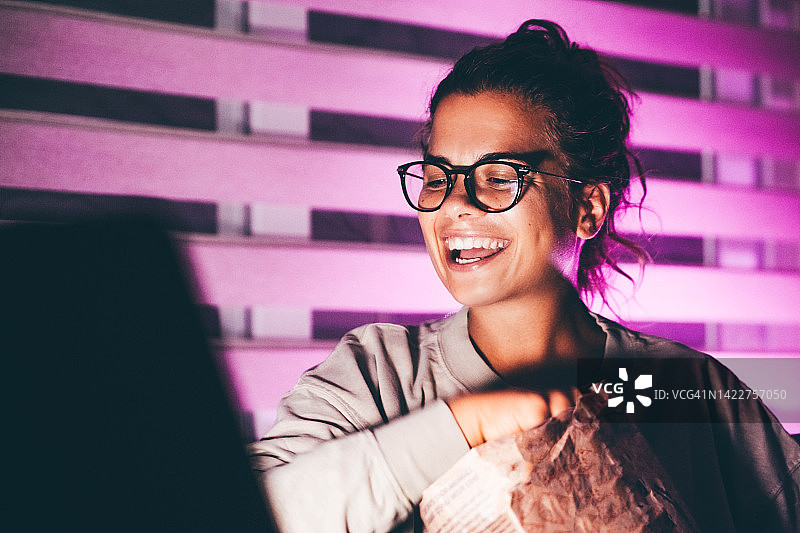 夜晚女人用笔记本电脑看电影吃玉米片图片素材