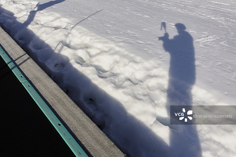 阳光明媚的日子里，滑雪者站在雪地上，手持滑雪杖的轮廓阴影图片素材