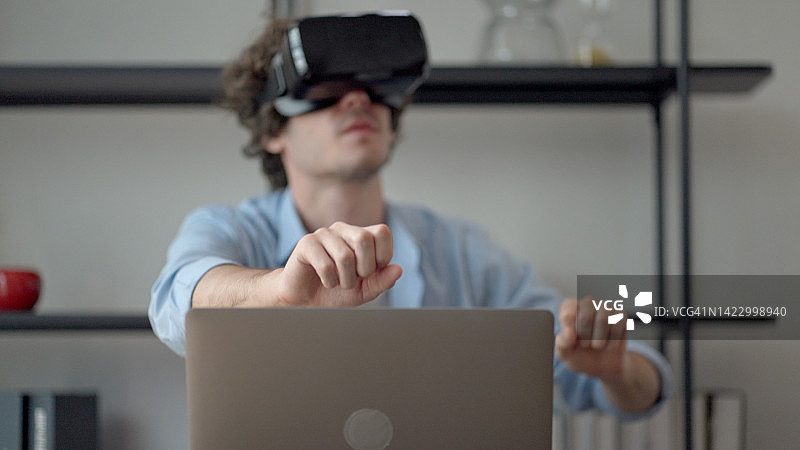 佩戴VR头显，在家通过在线系统远程学习的男大学生设计工程零件并发送给老师。图片素材