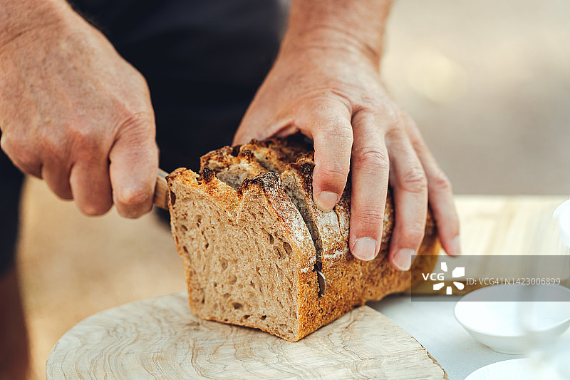 户外餐桌旁，年长男子切割面包特写图片素材