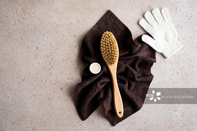 用于干刷按摩的木制身体刷、润肤霜、清洁手套和浴巾，混凝土背景，俯视图。家庭水疗概念。零浪费。平铺。复制空间。图片素材