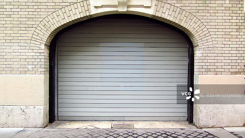 法国巴黎，受金属卷帘保护的车库入口，风化的砖石墙和人行道图片素材