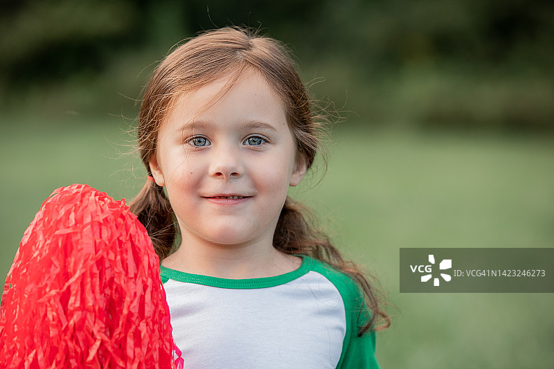 小女孩拿着绒球为团队欢呼，对着镜头微笑图片素材