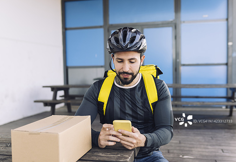坐着的送货员看着智能手机准备派送下一个包裹图片素材