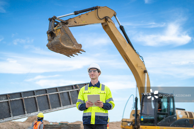 男工程师在建筑重型机械背景下使用平板电脑图片素材