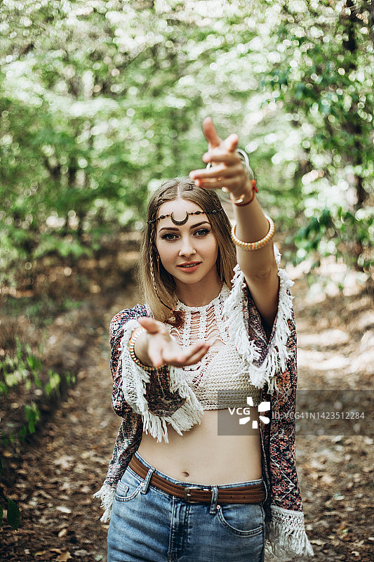 在阳光明媚的森林里做手势的年轻嬉皮士女子图片素材