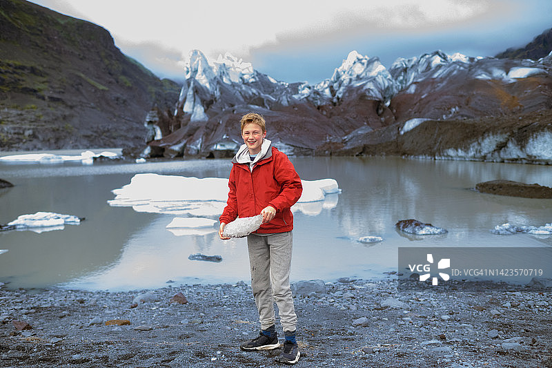 青少年男孩拿着冰川冰块，对着斯维纳冰川微笑图片素材