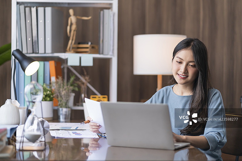 在客厅用笔记本电脑处理图表的亚洲微笑女性图片素材