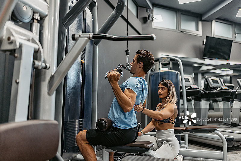 年轻女教练在健身房帮助年轻男人举重图片素材