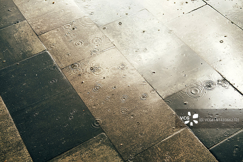 雨中湿滑的灰色路面，雨滴落入水坑图片素材