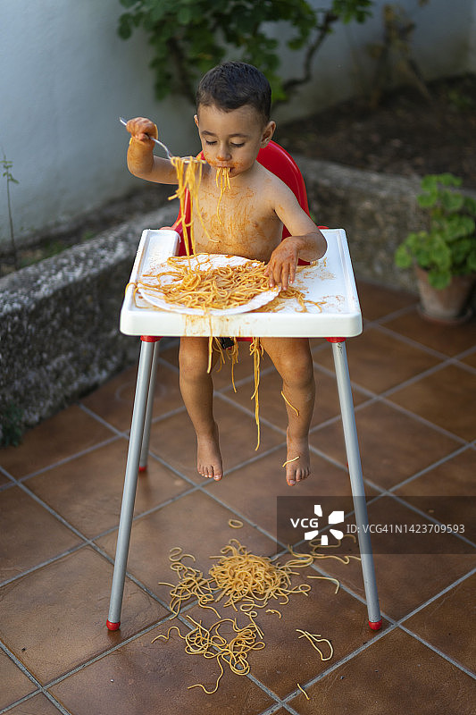 一岁宝宝坐在高脚椅上，身上沾满意大利面图片素材