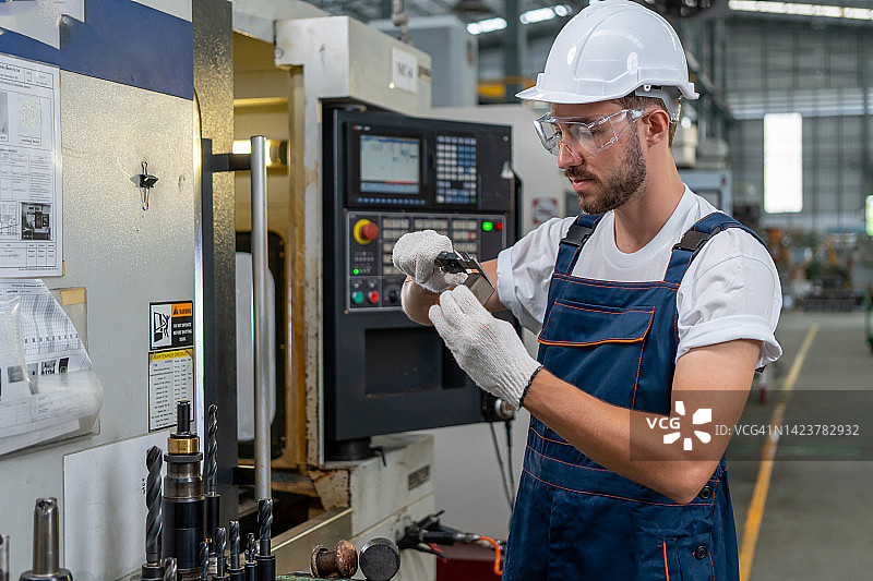 工厂工人正在使用平板电脑对数控铣床进行编程图片素材