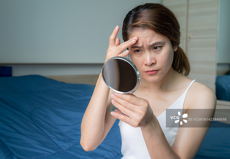 亚洲女人照镜子时担心脸上出现皱纹。图片素材