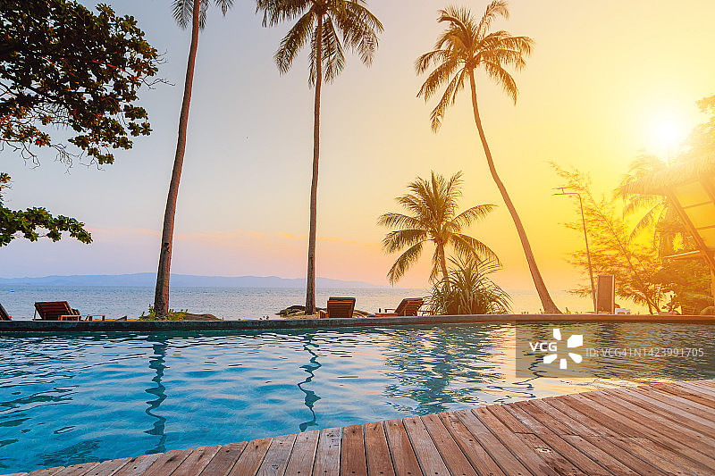 户外旅游景观：豪华海滩度假村，游泳池和沙滩椅在棕榈树和蓝天下，夏季旅游和度假背景概念图片素材