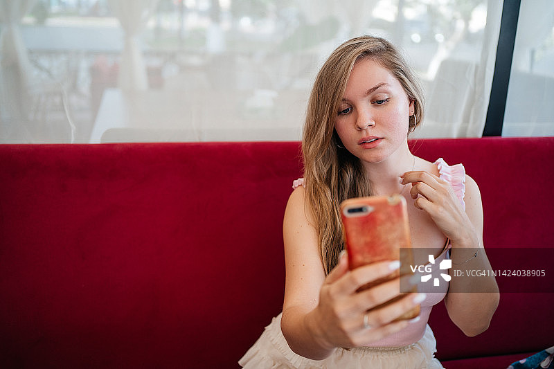 在咖啡馆用智能手机与朋友视频通话的女孩图片素材