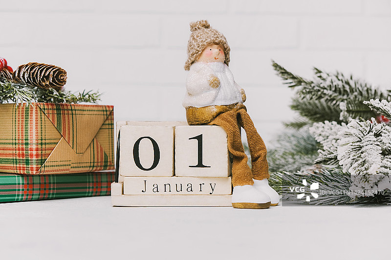 坐在1月1日积木旁的玩具侏儒，靠近礼物和冷杉树枝图片素材