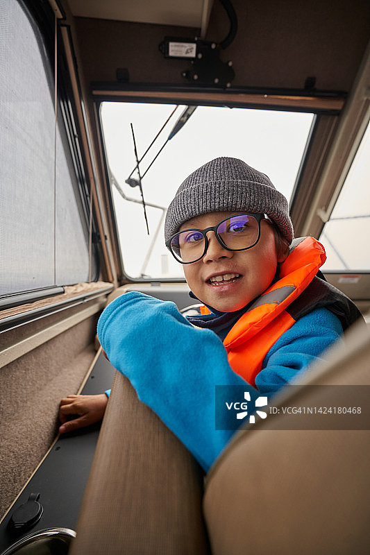 戴眼镜、穿救生衣、戴帽子的男孩在船上图片素材