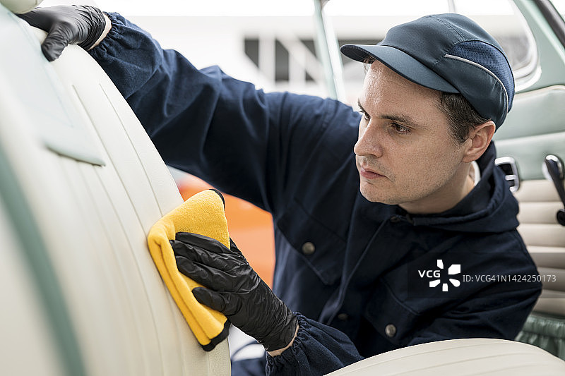 汽车内饰清洁服务：清除汽车座椅上的顽固污渍，汽车技术人员在汽车保养中心清洁、打蜡和擦拭，保护、涂层和消毒客户的汽车座椅图片素材