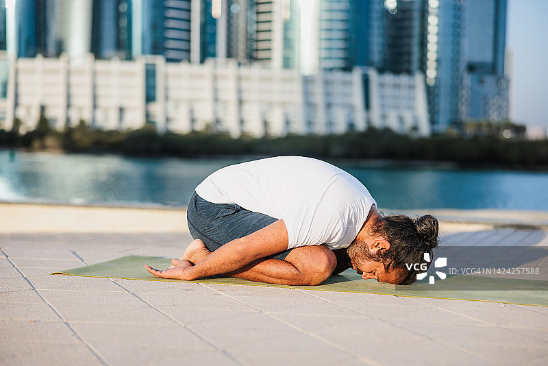 在阿布扎比码头上做瑜伽的男人，跪姿前屈图片素材