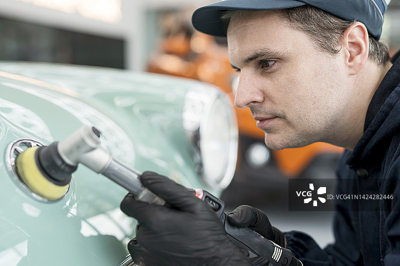 汽车维修中心：汽车机械师用抛光机修复汽车引擎盖图片素材