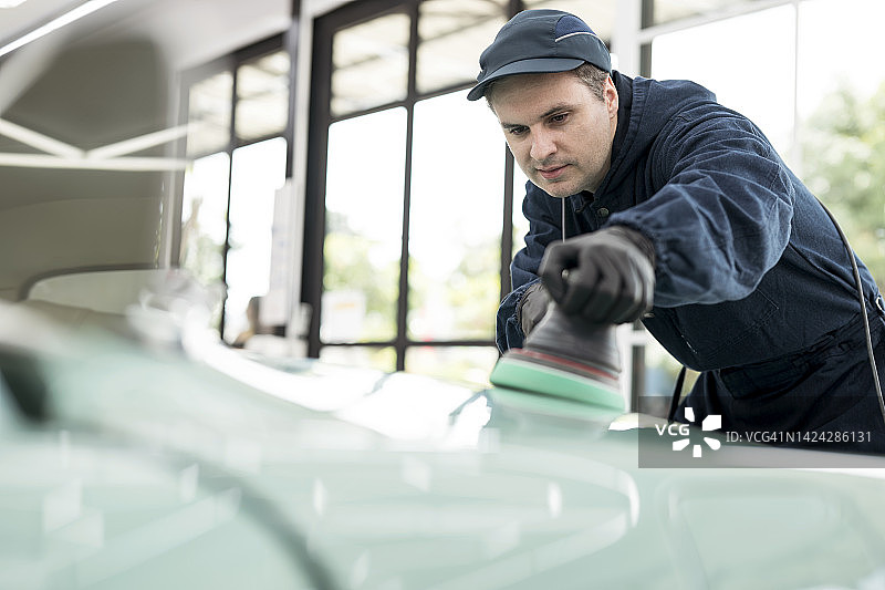 在车库修理经典汽车，用手持抛光机抛光汽车引擎盖外壳的修理工图片素材