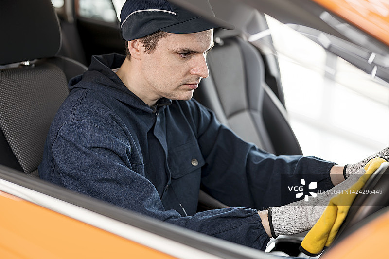 清洁方向盘、安全带、把手和其他汽车表面，对汽车内部进行消毒。汽车技术人员在汽车护理服务中心用柔软的黄色布清洁和擦拭顾客汽车的方向盘和整体设备。图片素材