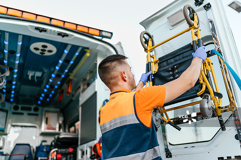 护理人员从救护车上取轮椅的背面照片图片素材